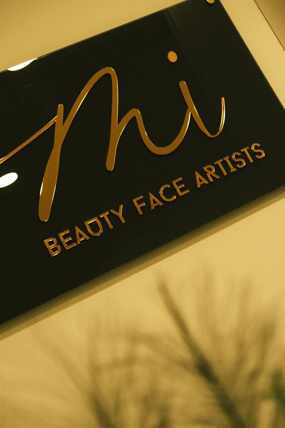 Черна табела в студиото със златен монограм на BeautyFace Artists, осветена от топла странична светлина.