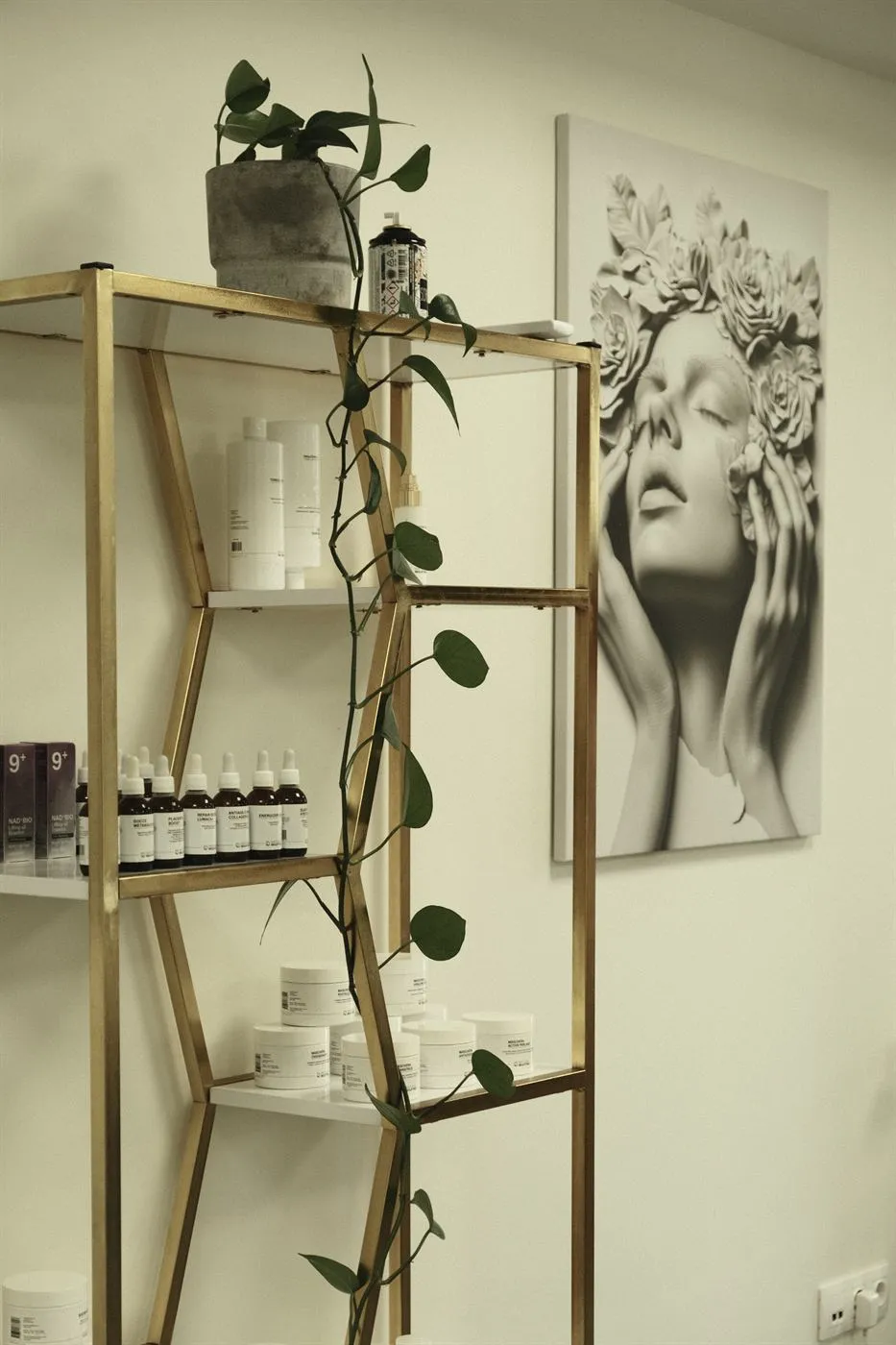 Златен рафт с ампули, маски и кремове NaturalBioLifting, увивно растение и картина с женско лице в цветя.