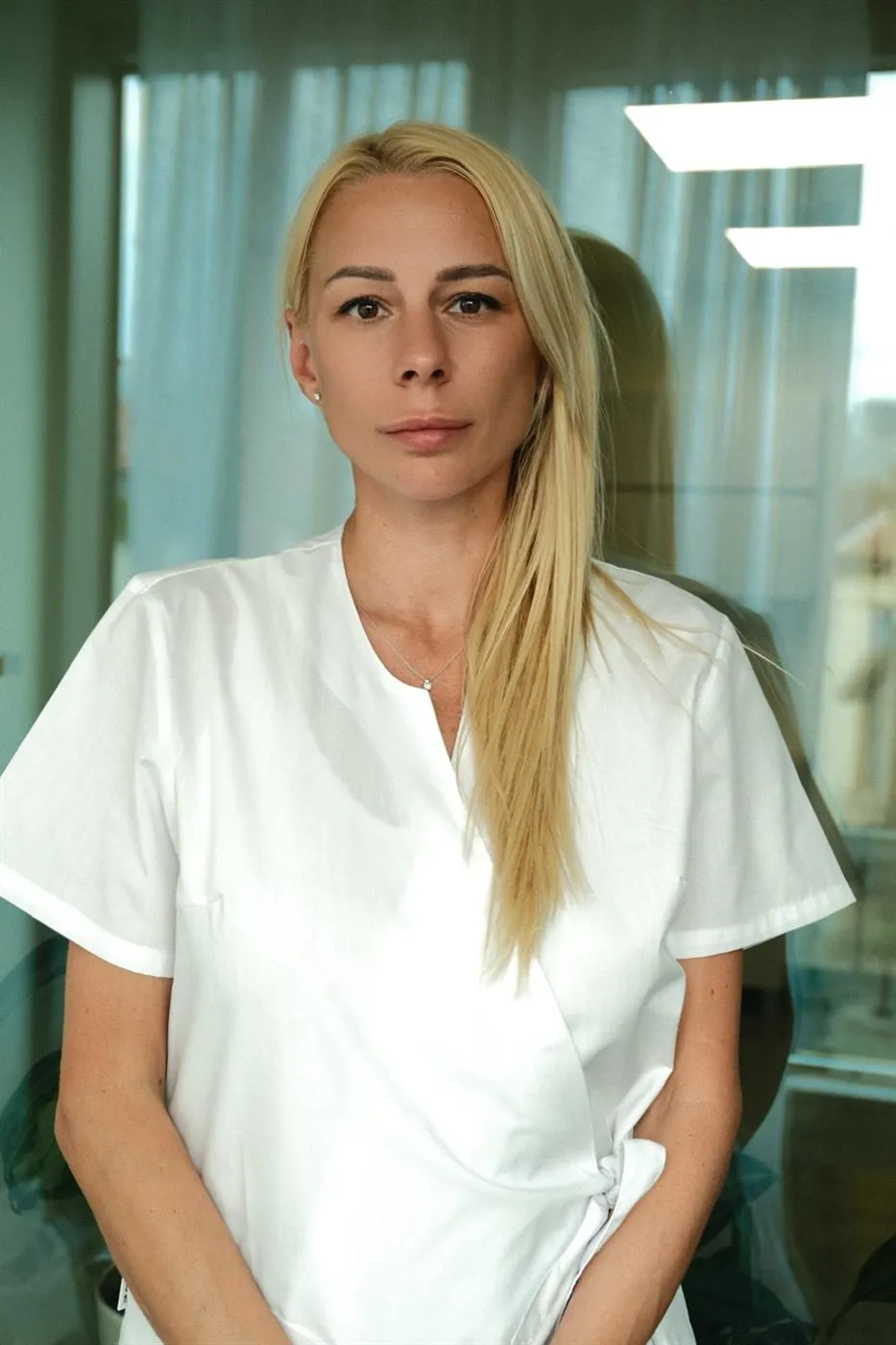 Мариела Иванова, създател на Beauty Face Artist, с дълга руса коса и бяла работна туника, застанала в кабинета на студиото.
