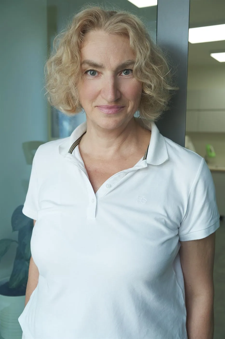 Терапевт за тяло в BeautyFace, с къса къдрава руса коса и бяла блуза с яка.